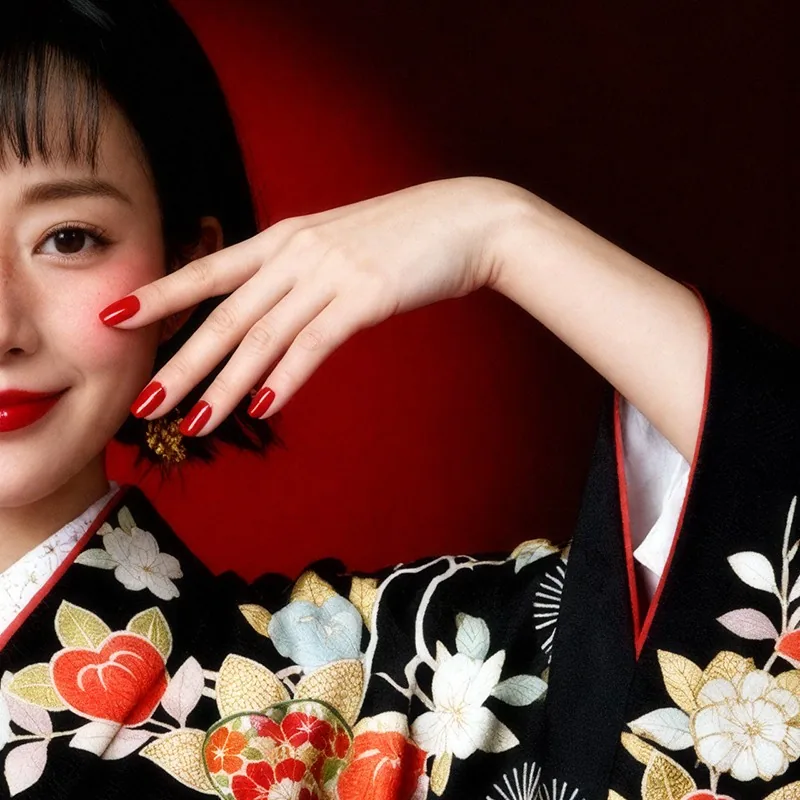 Woman in kimono with bold red lipstick and nails, poses with hands near her face with a smile.