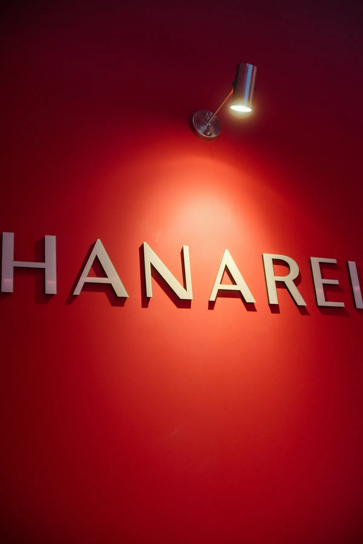 HANAREI nail salon sign on a red wall illuminated by a spotlight.